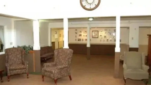 A large common area with multiple armchairs and a couch, a large wall clock, and a wall decorated with framed photos